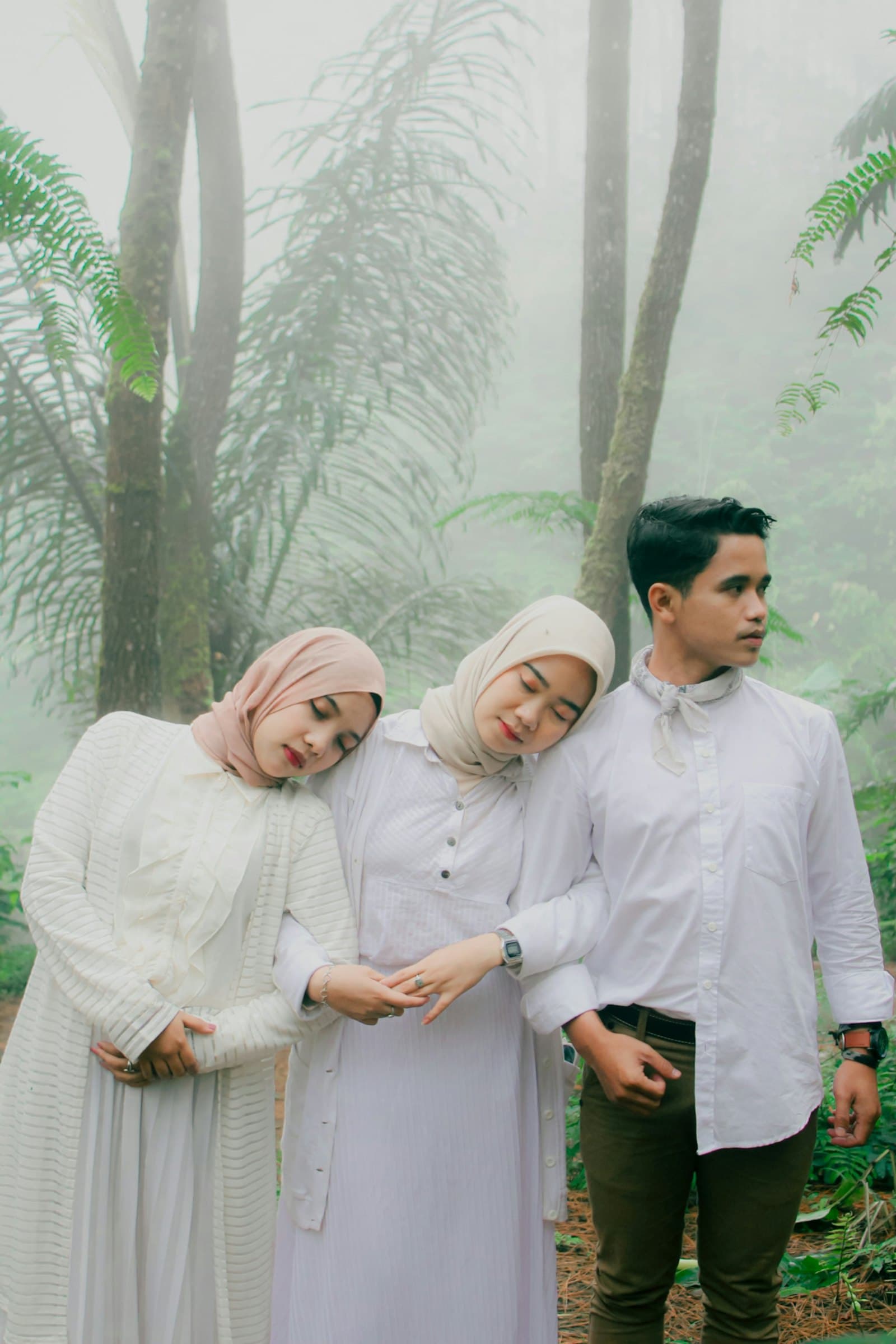 Tiga bersaudara berdiri berdampingan dengan tenang di taman yang berkabut.